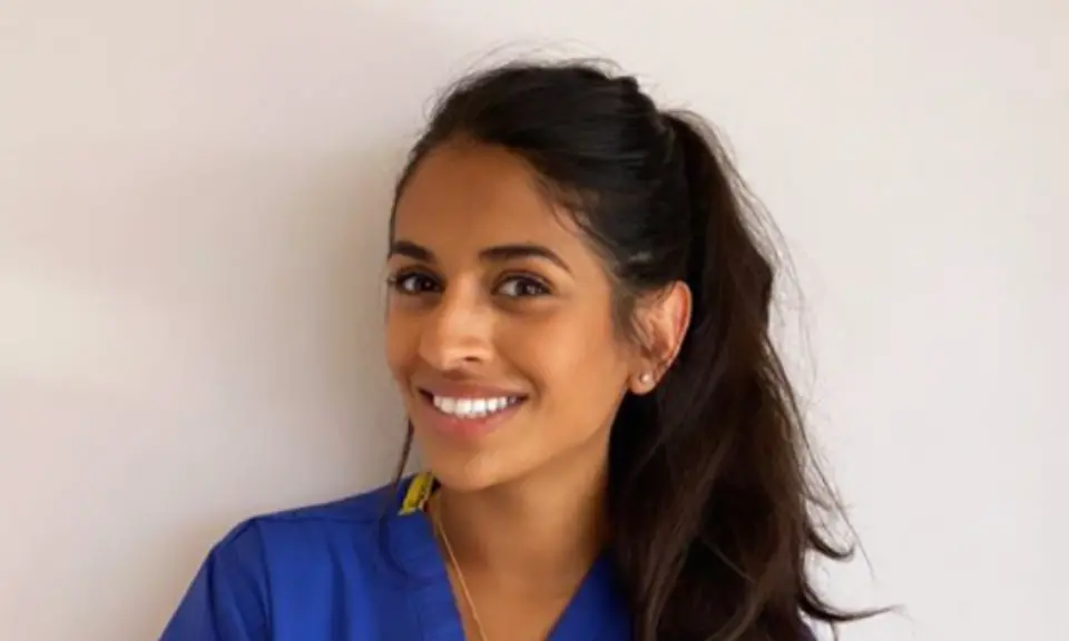 Dr. Priyanka Holzherr-Mandal, smiling, wearing blue surgical scrubs.