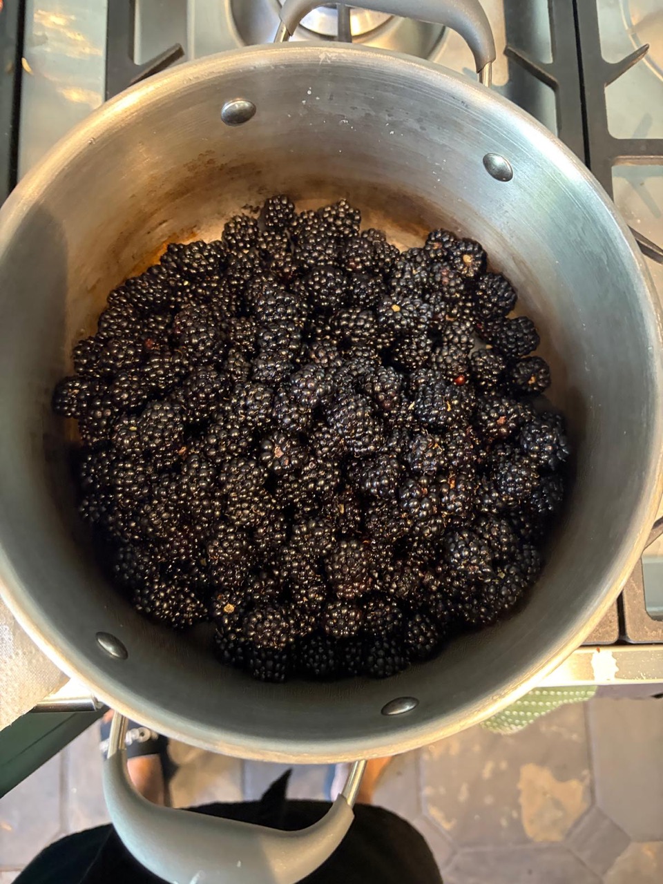 Overhead view of a steel saucepan on a gas hob, filled with fresh whole blackberries before cooking.