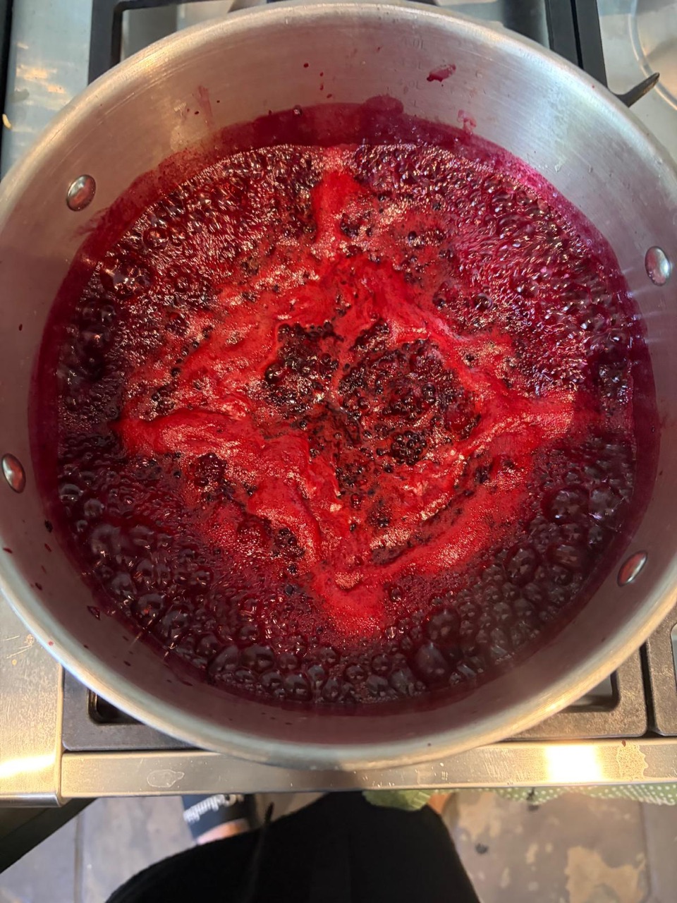 Overhead view of the same saucepan with the blackberries boiled down into a bubbling, bright red-purple jam.